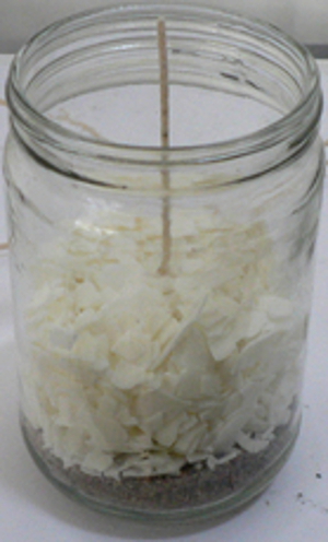A couple handfuls of soy wax flakes are placed around paraffin votive and wick